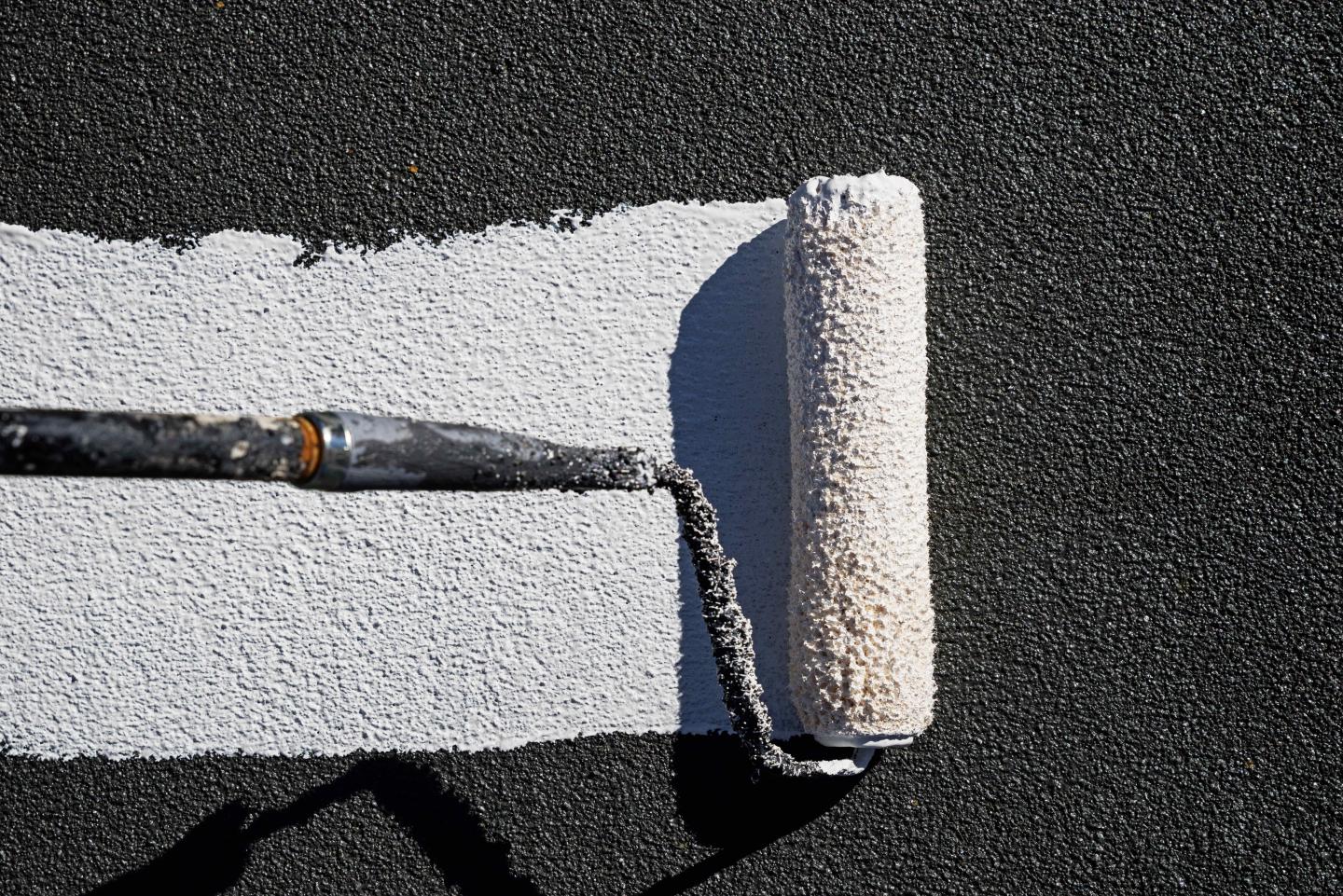 Paint roller painting dark asphalt white