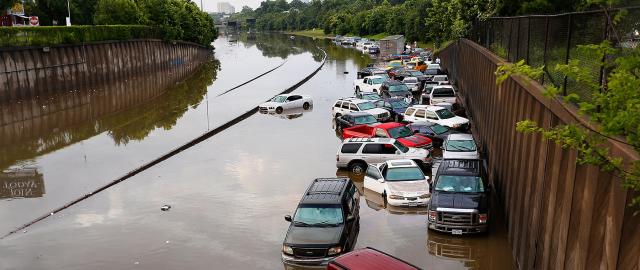 Cars on flooded highway with trees and buildings in the background