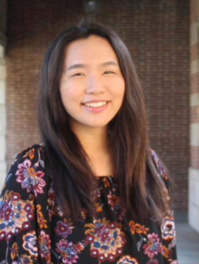 headshot of Maddy Tran in a darkly colored blouse with a tan stone building in the background