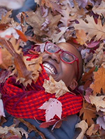Photo of Brittany Thomas smiling and covered in fall leaves.