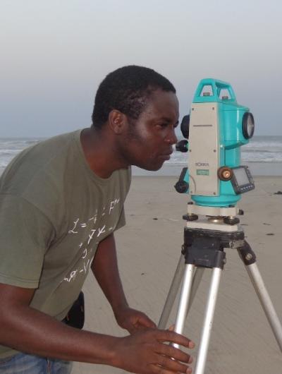 Photo of Ibrahim Amidu looking through a research device on a sandy beach. 
