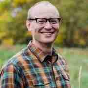 Headshot of Kevin Bright smiling with green field behind him