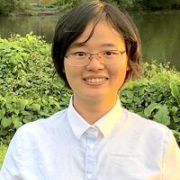 Headshot of Shijuan Chen in white blouse with foliage in the background