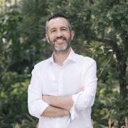 Headshot of Felipe Ramirez in a white shirt with foliage in the background