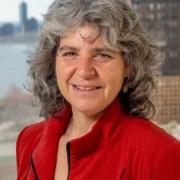 Headshot of Rachel Weinberger in a red blouse with a city skyline in the background