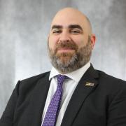 Headshot of Garrett Eucalitto in a black blazer against a gray background