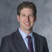 Headshot of David Kooris in a dark blue blazer against a gray background