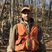 Headshot of Max Piana in orange vest with woods in background