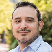 Headshot of Michael Rodriguez in a blue shirt with foliage in the background