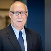 Headshot of David Vlahov in a suit against blue and brown background