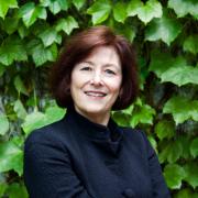 Headshot of Diane Davis in dark blue blazer with ivy in the background