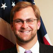 Headshot of Doug Hausladen against American flag background