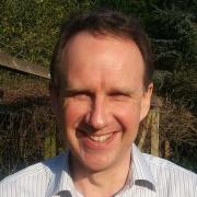 Headshot of William Bird in white shirt with garden wall in the background