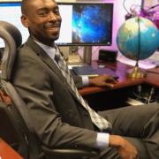 Gerald Bright sitting in a desk chair with globe in the background