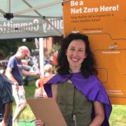 Jillian Wilson-Martin standing with a clipboard in front of a poster that says "Be A Net Zero Hero!"