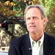 Headshot of John Wargo in dark suit with fall foliage in the background