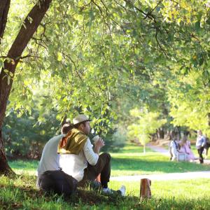 Person in white shirt and jeans sitting on sunny patch of grass under trees