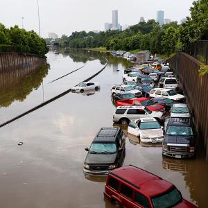 Cars on flooded highway with trees and buildings in the background